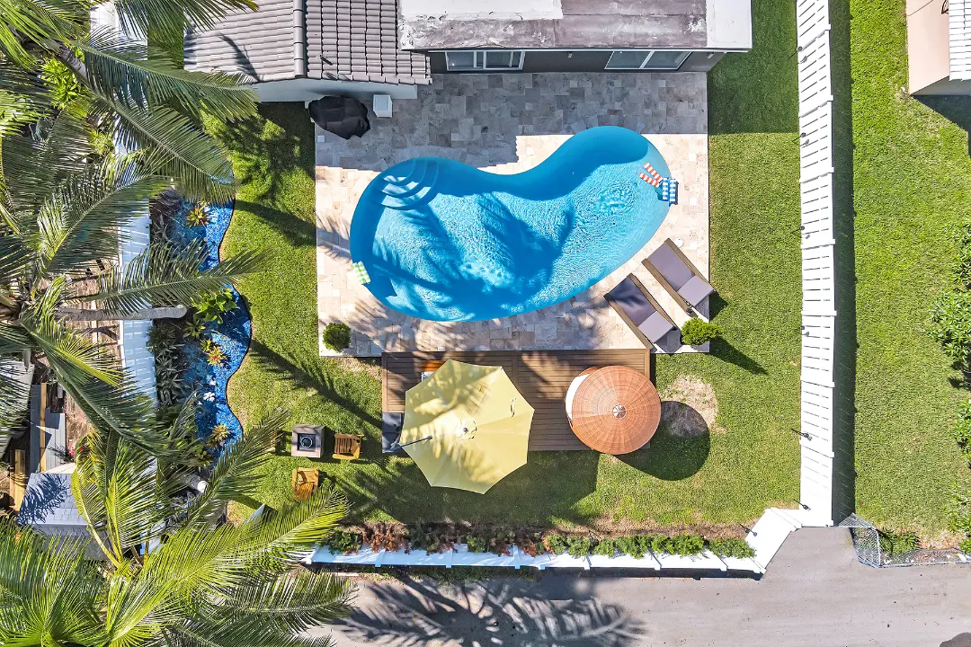 Aerial view of landscaped backyard with curved pool, deck seating, and umbrella featured in our About Us section.