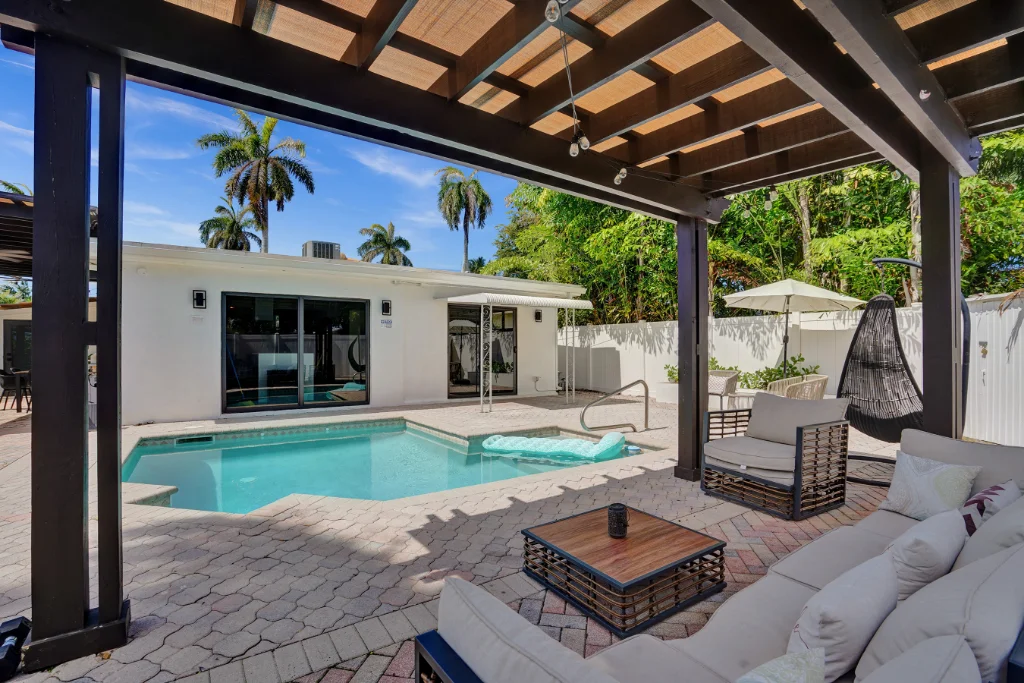 Covered patio seating area overlooking a backyard pool with palm trees and lounge chairs.