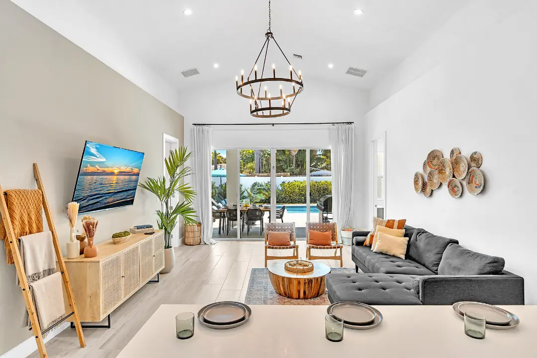 Bright living room with chandelier, TV, and glass doors opening to pool patio in a long-term rental property.