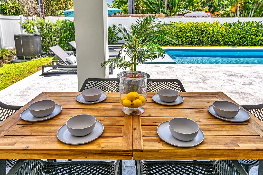 Outdoor dining table set for six on covered patio overlooking pool in a managed long-term rental.