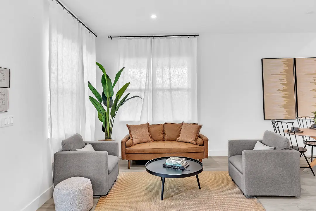 Cozy sitting area with tan loveseat, two gray chairs, and indoor plant in a long-term managed rental.