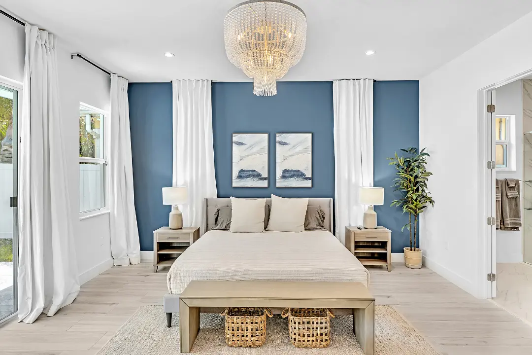 Bright bedroom with blue accent wall, chandelier, neutral bedding, and matching nightstands