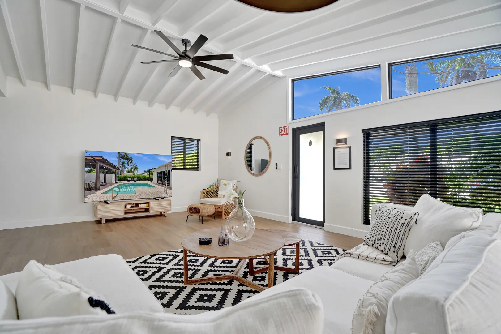 Stylish living room with white sofa, round mirror, and large TV displaying an outdoor pool area