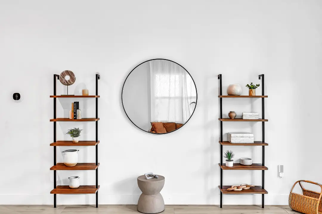Decorative wall with twin wooden shelves and large round mirror in a professionally managed rental home.