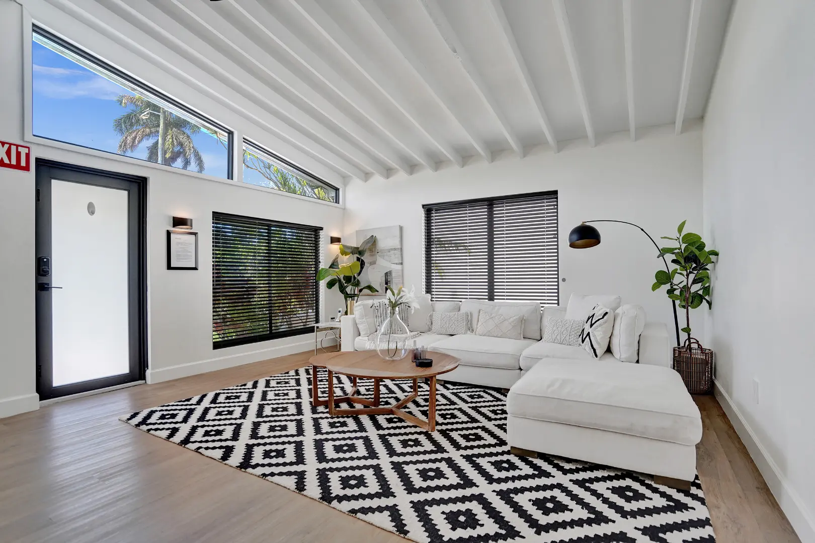 Bright modern living room with white sectional sofa, black blinds, and geometric rug under vaulted ceiling in South Florida
