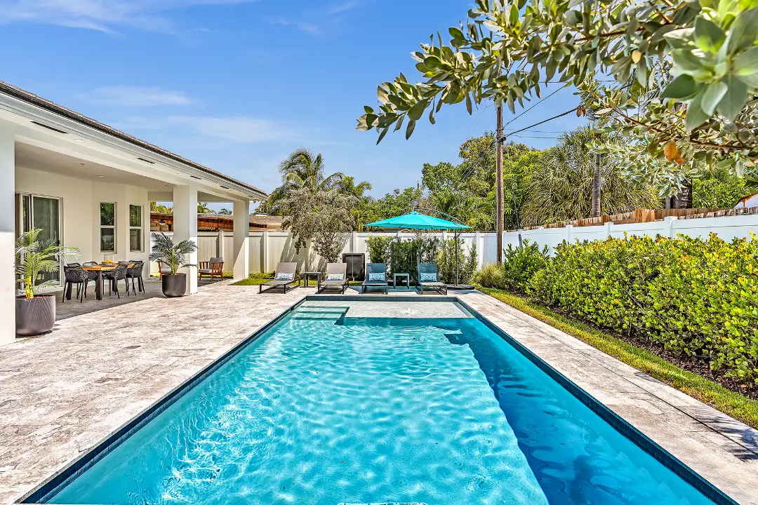 Backyard pool with loungers, umbrella, and tropical landscaping at a managed vacation rental.