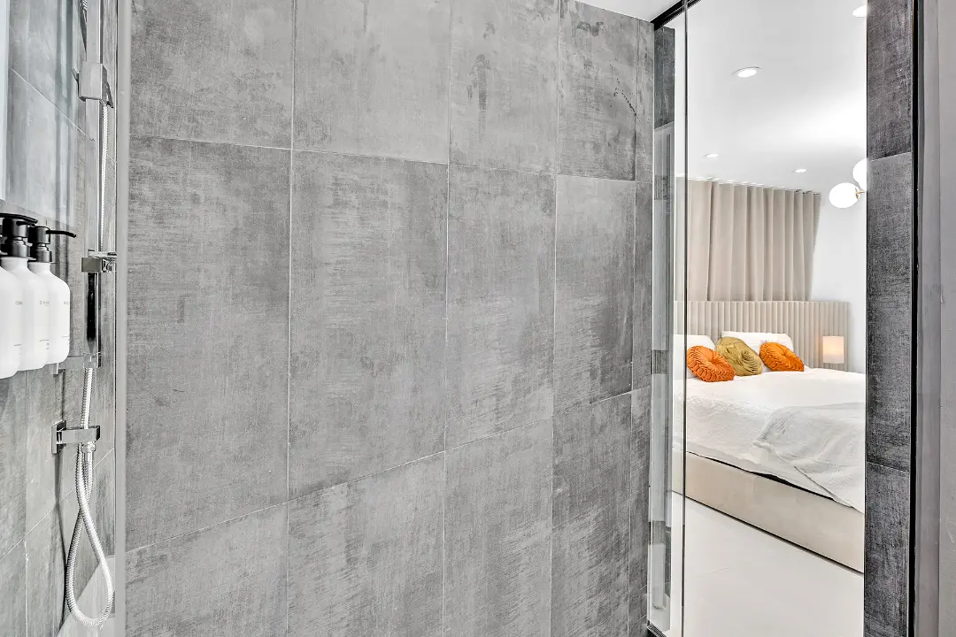 Large gray-tile shower with view into a well-appointed vacation rental bedroom.