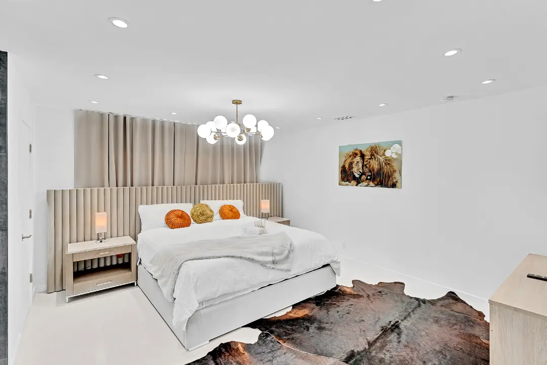 Modern vacation rental bedroom with padded headboard, globe chandelier, and neutral décor.