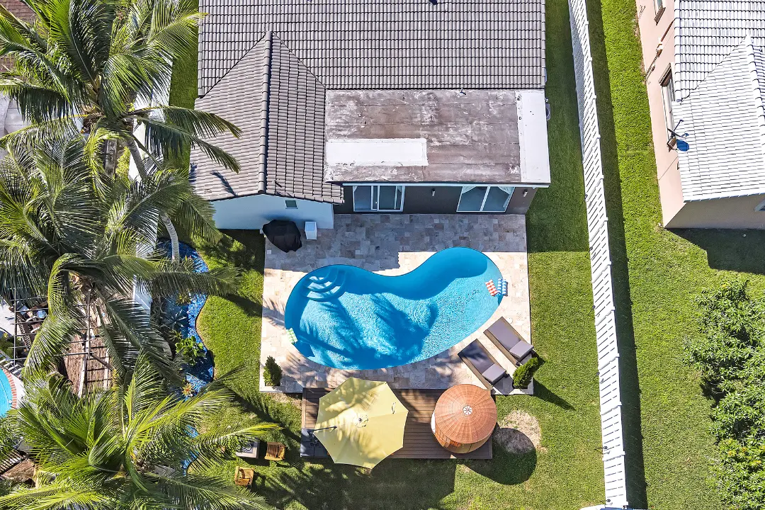 Aerial view of vacation rental home with curved pool, patio deck, and palm landscaping.